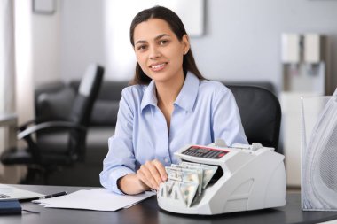 Kadın banka müdürü ofiste para sayma makinesi kullanıyor.