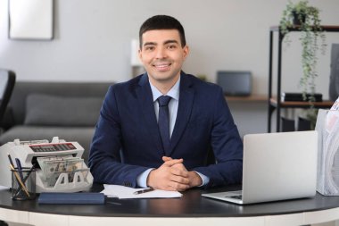 Erkek banka müdürü ofiste para sayma makinesiyle çalışıyor.