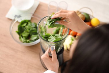 Genç bir kadın mutfakta ıspanağı blender 'a koyuyor, yakın plan.