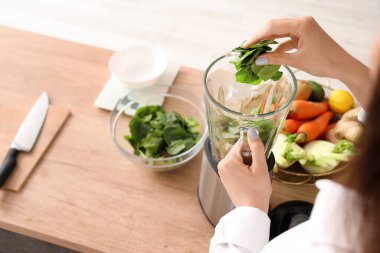 Genç bir kadın mutfakta ıspanağı blender 'a koyuyor, yakın plan.