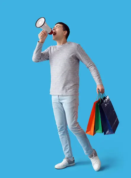 Молодой Человек Пакетами Покупок Кричит Мегафон Синем Фоне — стоковое фото
