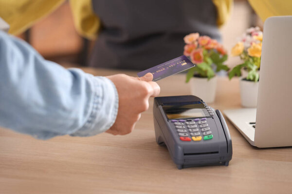 Young man paying with credit card via payment terminal in flower shop, closeup