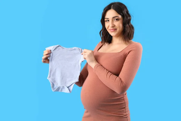 若いです妊娠中の女性とともに赤ちゃんボディスーツ上の青の背景 — ストック写真