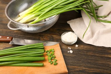 Board with fresh green onion on wooden background