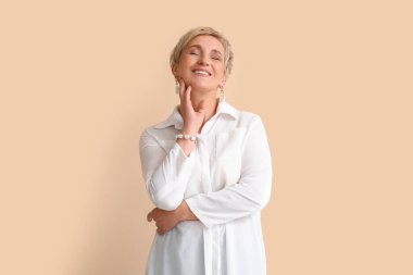 Bej arka planda beyaz gömlekli olgun sarışın kadın.