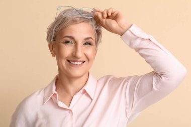 Bej arka planda gözlüklü olgun sarışın kadın, yakın plan.