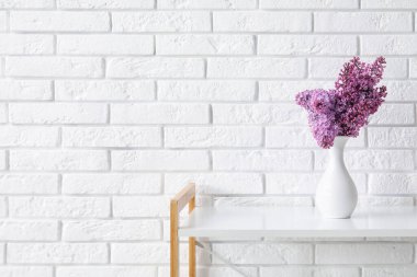 Açık tuğla duvarın yanındaki masada güzel leylak çiçekleri olan vazo