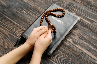 Dua boncuklu kadın elleri ve ahşap arka planda kutsal İncil.