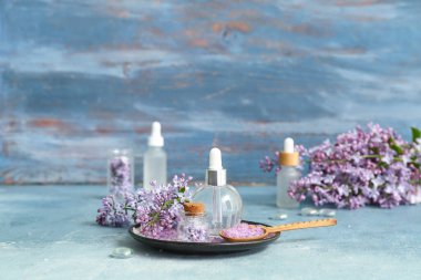 Güzel leylak çiçekleri ve mavi masanın üzerinde deniz tuzu olan kozmetik yağları.