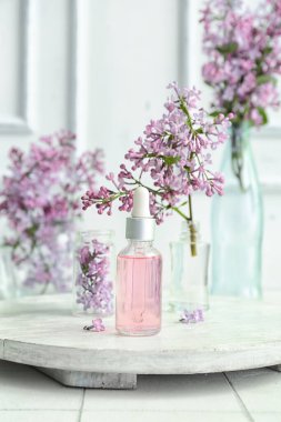 Beyaz masa üzerinde güzel leylak çiçekleri olan kozmetik yağı şişeleri.