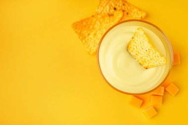 Lezzetli çedar peyniri soslu kase ve sarı arka planda nacho.