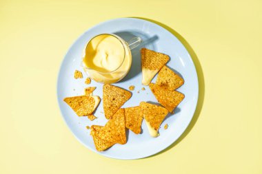 Bir sürahi lezzetli çedar peyniri sosu ve soluk sarı arka planda nachos.