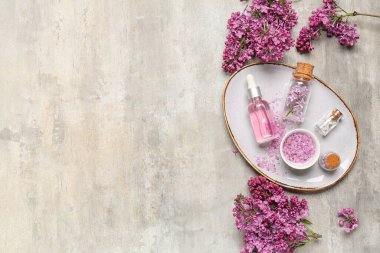 Bir şişe leylak yağı, deniz tuzu ve arkaplanda çiçekler.