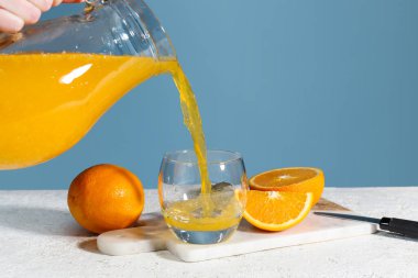 Taze portakal suyunu sürahiden bardağa dökerek mavi arkaplana karşı masaya döker.