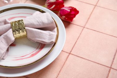 Katlanmış peçete, çatal bıçak takımı ve pembe fayanslı lale çiçekli tabaklar.