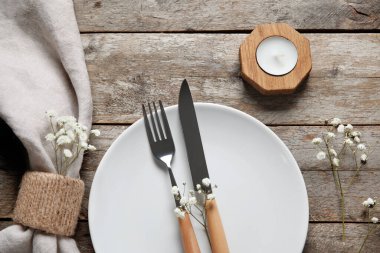 Kahverengi ahşap arka planda katlanmış peçete, çatal bıçak ve mum tabağı.