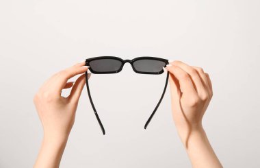 Beyaz arka planda şık güneş gözlüğü tutan kadın eller.