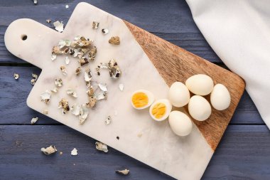 Kaynamış bıldırcın yumurtaları ve mavi ahşap arka planda kabuklar.