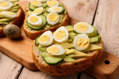 Hafif ahşap arka planda bıldırcın yumurtası, avokado ve salatalıklı lezzetli tostlar, yakın plan.