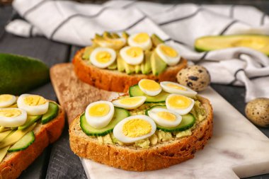 Bıldırcın yumurtalı lezzetli tostlar, avokado ve salatalık koyu ahşap arka planda, yakın plan