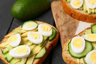 Bıldırcın yumurtalı lezzetli tostlar, avokado ve salatalık koyu ahşap arka planda, yakın plan
