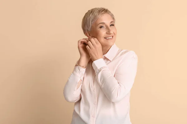 Mature blonde woman with earrings on beige background