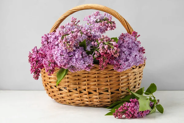 stock image Wicker basket with aromatic lilac flowers on light table