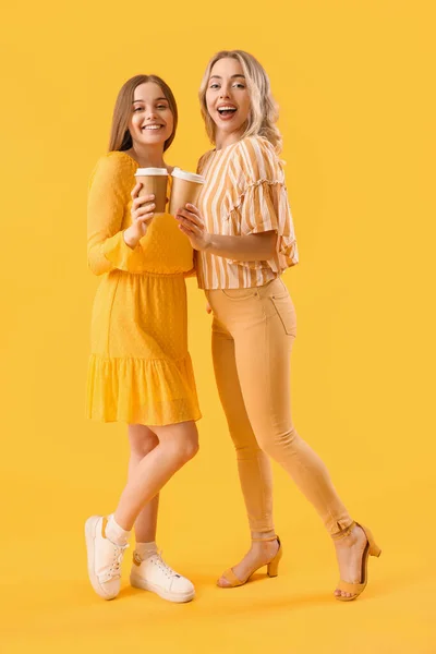 Junge Schwestern Mit Tassen Kaffee Auf Gelbem Hintergrund — Stockfoto
