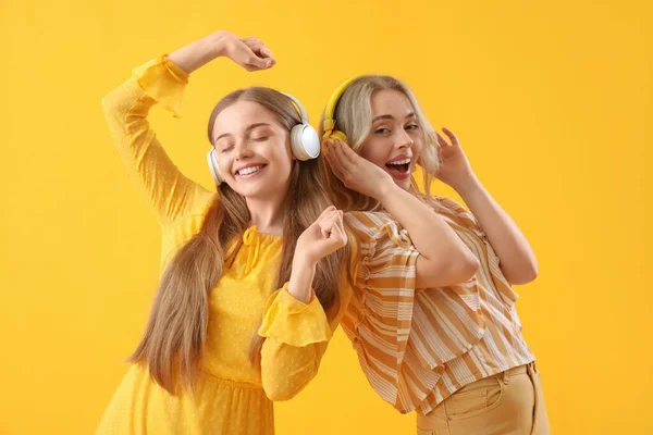 stock image Young sisters in headphones dancing on yellow background