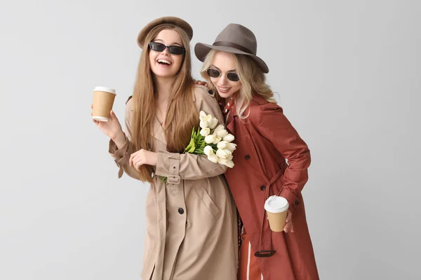 stock image Young sisters with cups of coffee and tulips on light background