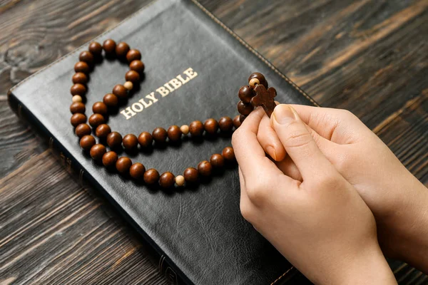 Mãos Femininas Com Contas Oração Bíblia Sagrada Fundo Madeira — Fotografia de Stock