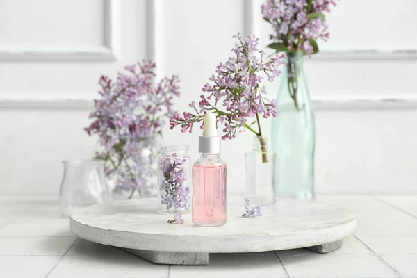 白いテーブルの上に美しいライラックの花と化粧品油のボトル — ストック写真