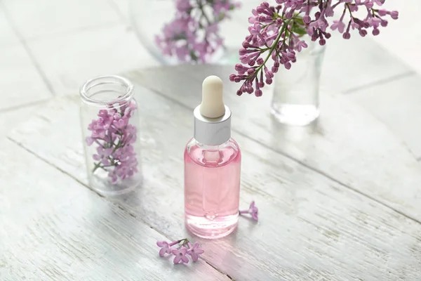 Bottles of cosmetic oil with beautiful lilac flowers on white table