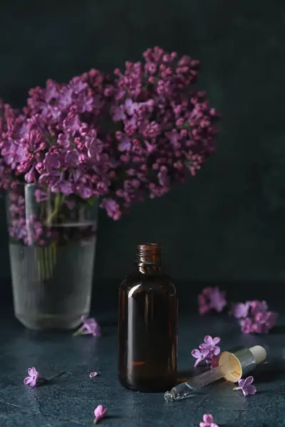 Fles Cosmetische Olie Met Mooie Lila Bloemen Donkere Tafel — Stockfoto
