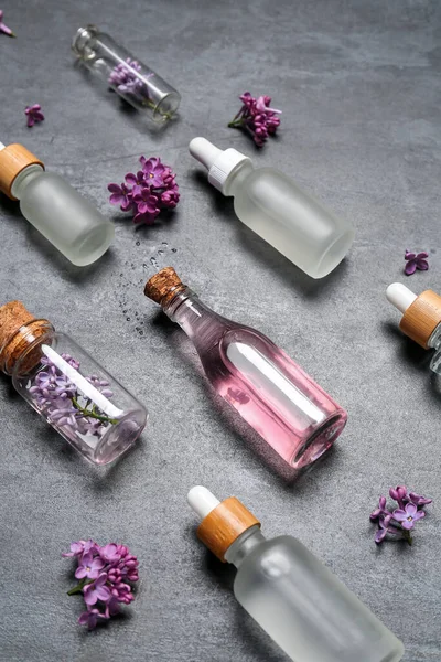 Bottles of lilac essential oil and flowers on dark background, closeup
