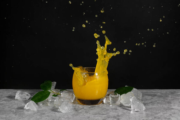 Glass of fresh orange juice with splashes and ice on dark background