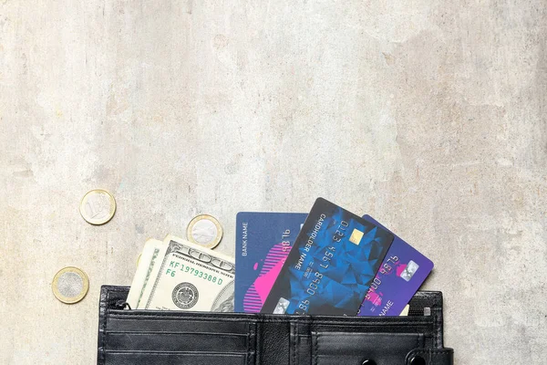 Black wallet with money, credit cards and coins on beige grunge table