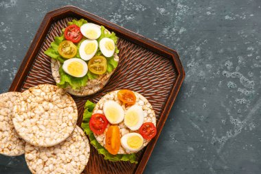 Üzerinde bıldırcın yumurtası, domates ve marul olan pirinç krakerleri.