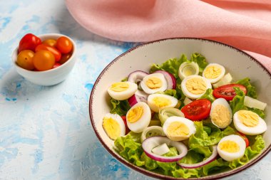 Açık mavi arka planda bıldırcın yumurtalı, domatesli, soğanlı ve marullu lezzetli salata.