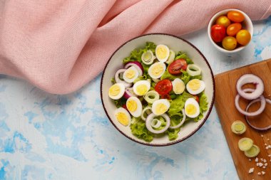 Bıldırcın yumurtalı, domatesli, soğanlı ve açık mavi arkaplanlı lezzetli salata.