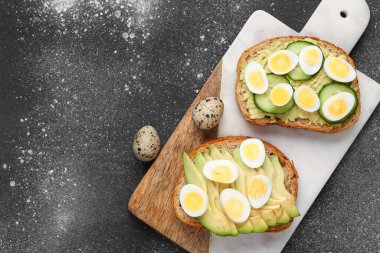 Bıldırcın yumurtalı lezzetli tostlar, avokado ve koyu grunge arka planda salatalık.