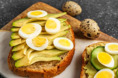 Bıldırcın yumurtalı lezzetli tostlar, avokado ve salatalık koyu grunge arka planda, yakın plan