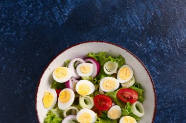 Bıldırcın yumurtalı, domatesli, soğanlı ve lacivert arkaplı lezzetli salata.