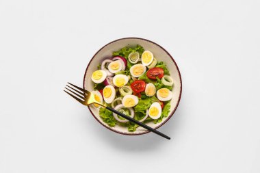 Beyaz arka planda bıldırcın yumurtalı, domatesli, soğanlı ve marullu lezzetli salata.