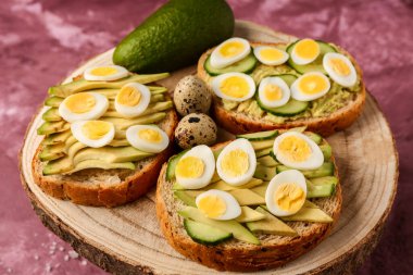 Pembe arka planda bıldırcın yumurtası, avokado ve salatalıklı lezzetli tostlar, yakın plan.