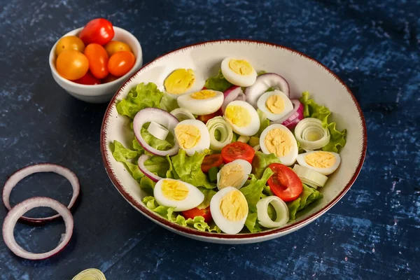 stock image Tasty salad with quail eggs, tomatoes, onion and lettuce on dark blue background