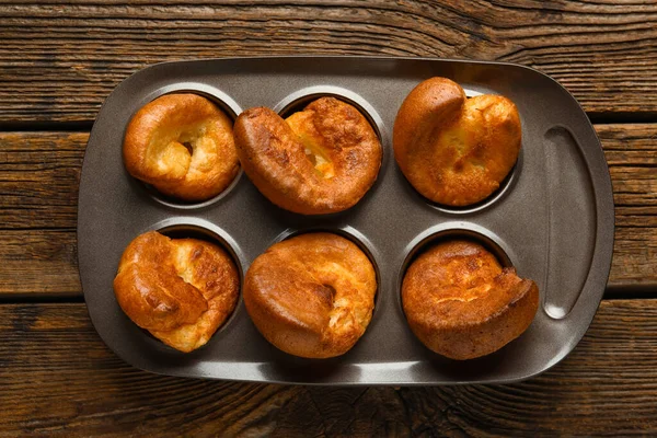 Ahşap arka planda lezzetli Yorkshire pudingi olan teneke fırın.