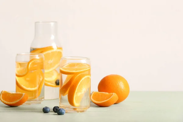 薄い木製のテーブルの上にオレンジのスライスと注入水のグラスとボトル — ストック写真