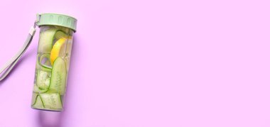 Bir şişe salatalık, eflatun arkaplan üzerine serpiştirilmiş su, metin için alan, üst görünüm