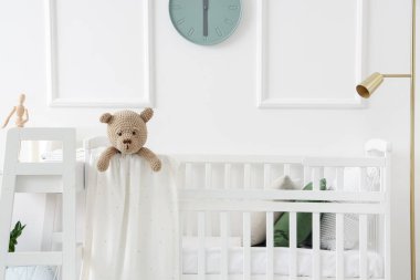 Baby crib with toy bear in light bedroom